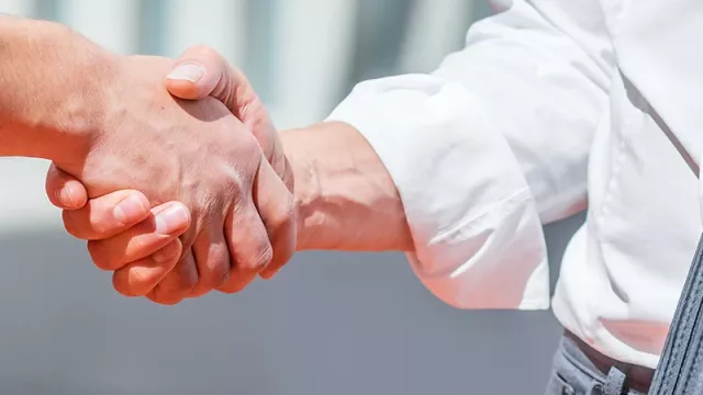 Two men shake hands. One is wearing installer's clothing. The other is wearing business attire.