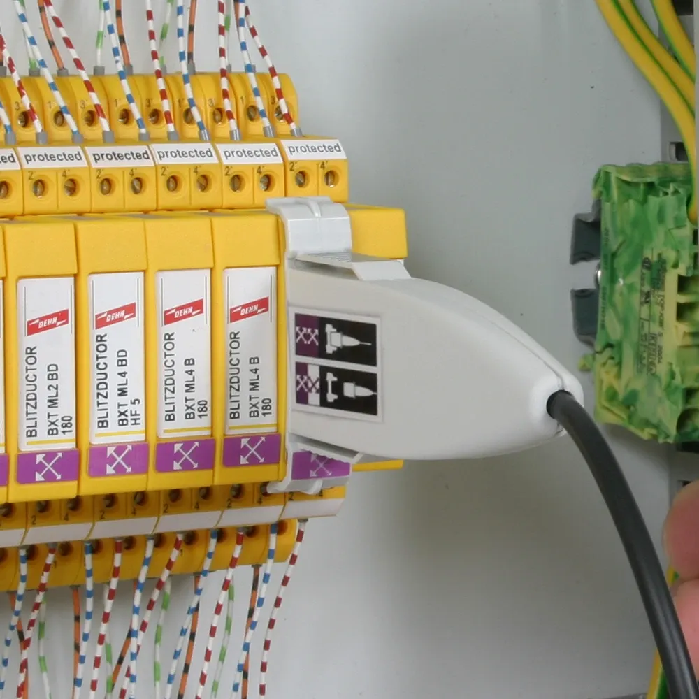 White test adapter plugged into a yellow surge protection module inside an electrical control cabinet with connected wires.