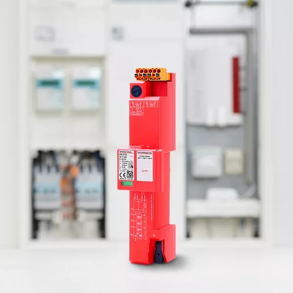 A red electronic device with various connectors is displayed in the foreground, with blurry electrical components in the background.